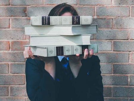 the student is holding books that cover her face